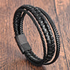 Close up view of a black braided leather bracelet with a rectangular metal clasp on a wooden surface