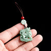 Light green jade Kirin carving hanging from a brown cord with a red bead and white coin.