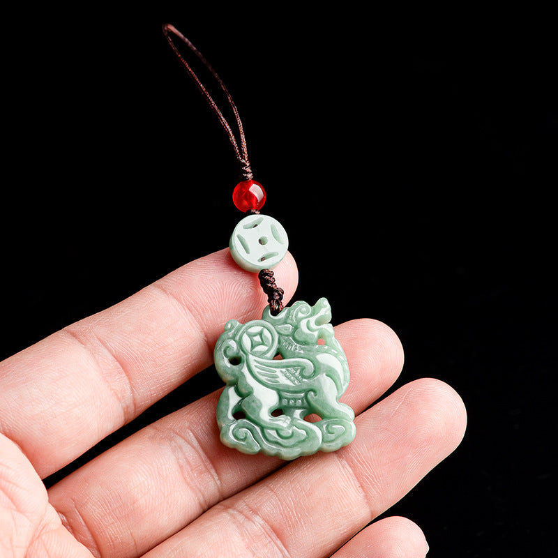 Light green jade Kirin carving hanging from a brown cord with a red bead and white coin.