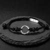 Close up of a black cord bracelet with a silver ring charm and black beads on a stone surface