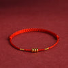 Close-up of a red braided cord bracelet with gold-tone abacus beads against a warm background