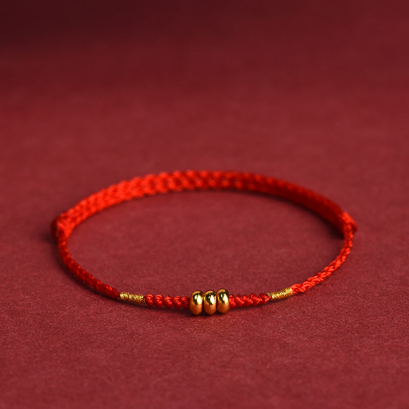 Close-up of a red braided cord bracelet with gold-tone abacus beads against a warm background