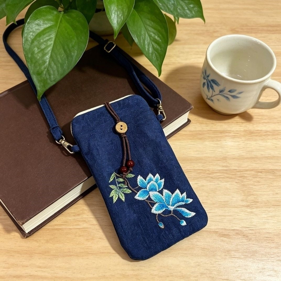 Navy blue embroidered crossbody bag with blue lotus design resting on a book next to a cup of tea