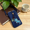 Navy blue embroidered crossbody bag with blue lotus design resting on a book next to a cup of tea