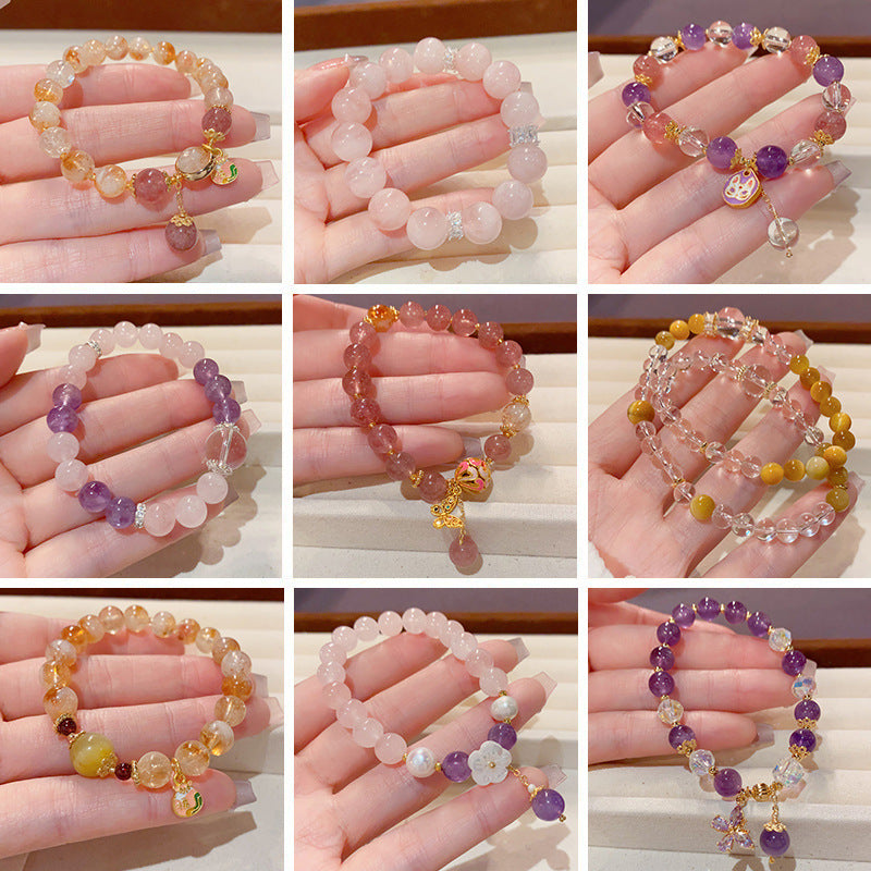Hand holding a beaded crystal bracelet with purple and pink stones and a gold charm