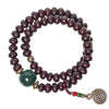 Brown bodhi seed bracelet with green bead and spiral charm on red clay surface